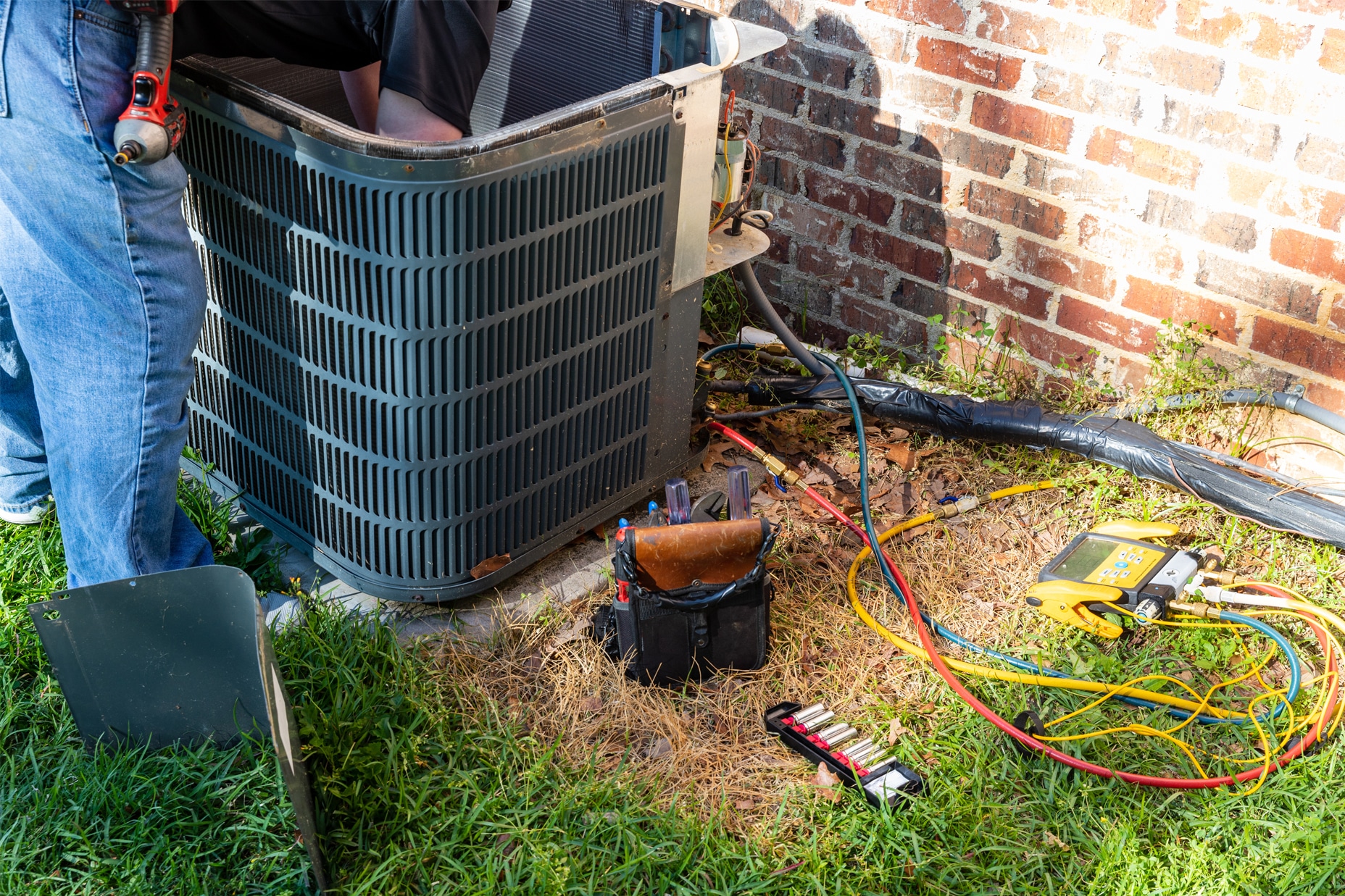 Pat Green Heating & Cooling tech repairing an ac unit outside a brick home