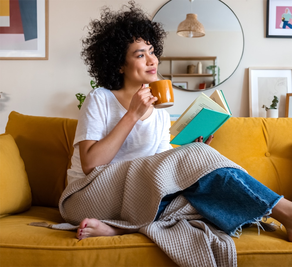 Young woman enjoying a cup of coffee and reading a book on an orange couch